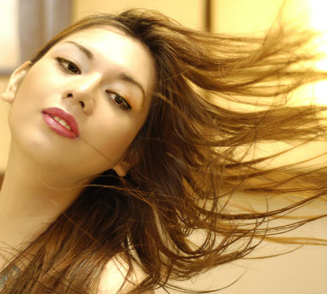 A close-up portrait in warm light, long brown hair caught mid-motion across the face